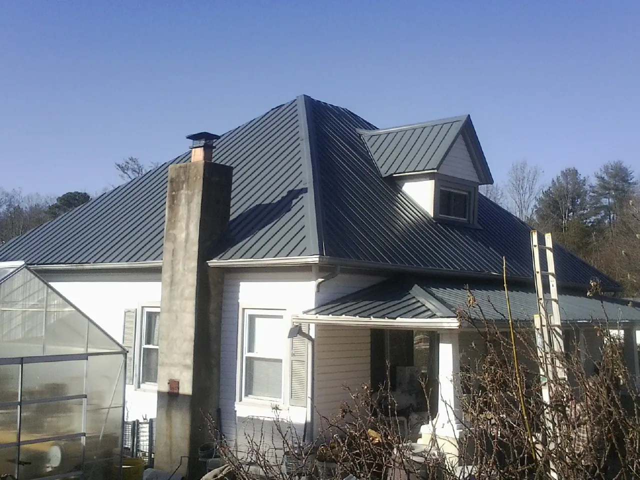 Dark blue standing seam metal roof on a white farmhouse with dormer — Slate & Tile Roof Repair by Roofing Brothers in Quinton
