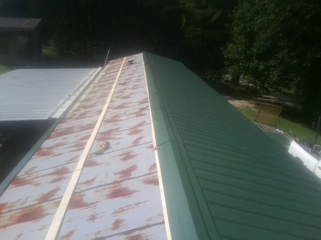 Old rusted panels beside newly installed green metal roofing — Wind Damage Roof Repair by Roofing Brothers in Quinton