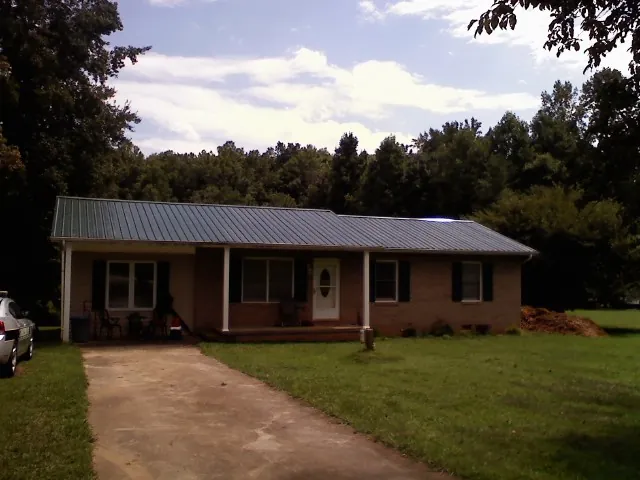 Dark green metal roof on a brick ranch with a covered porch in Quinton
