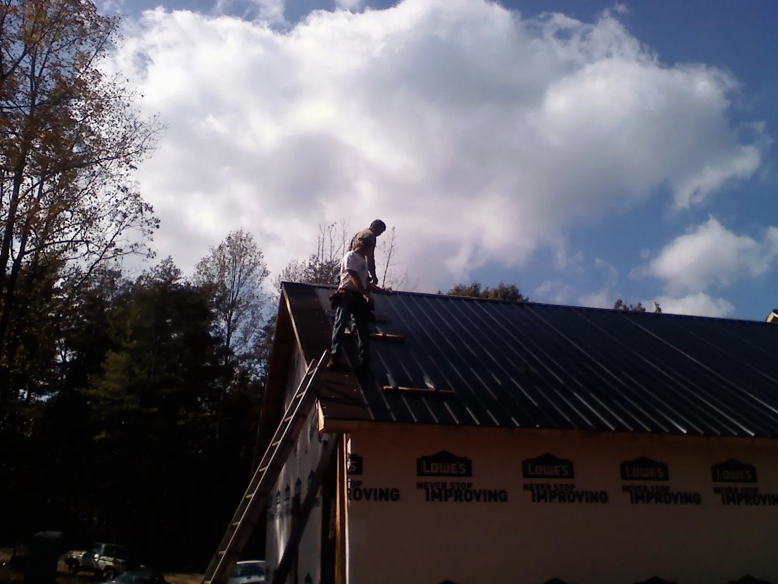 Roofer fastening dark metal panels high against a cloudy sky, from a Roof Inspection job in Quinton